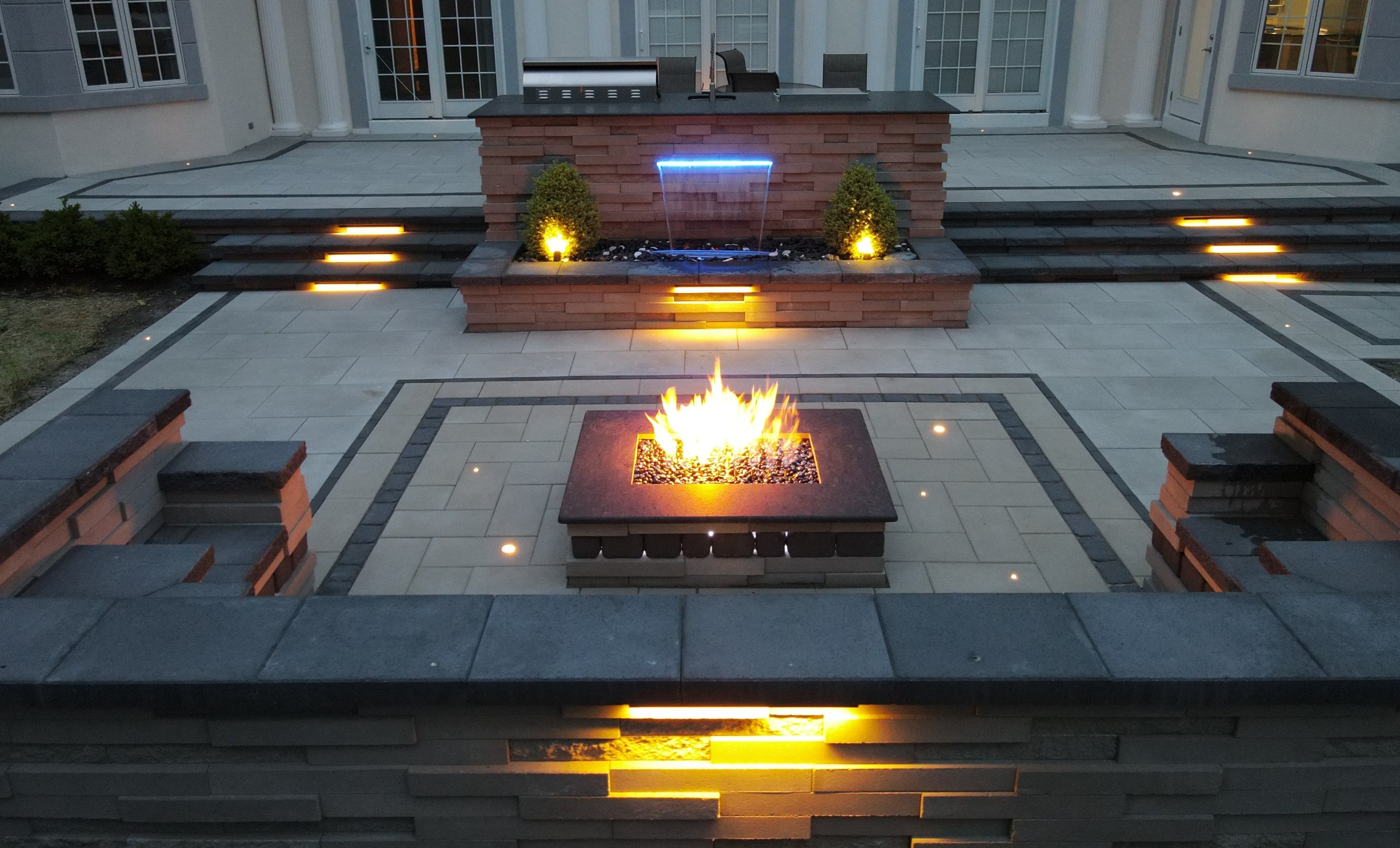landscape design/build firm in Bellevue installed a paver patio with charcoal border, landscape lighting, firepit, water feature, block wall, sitting wall, and pavers patio
